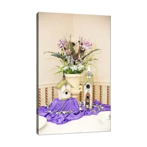 Rabatt Canvastavla 70x100 cm - Vacker blomsterarrangemang i en kruka med två fågelhus på en lila duk Lila / Grön / Vit - Inredning