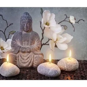 Köp nu Canvastavla 70x100 cm - Sittande Buddha omgiven av blommor och stenar med tända ljus Grå / Vit / Beige - Inredning